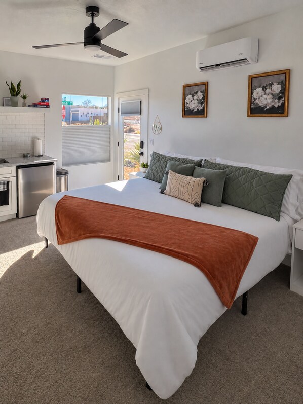 Un dormitorio con cama, almohadas, ventilador de techo, equipo de aire acondicionado, ventana con vistas y una zona de kitchenette.