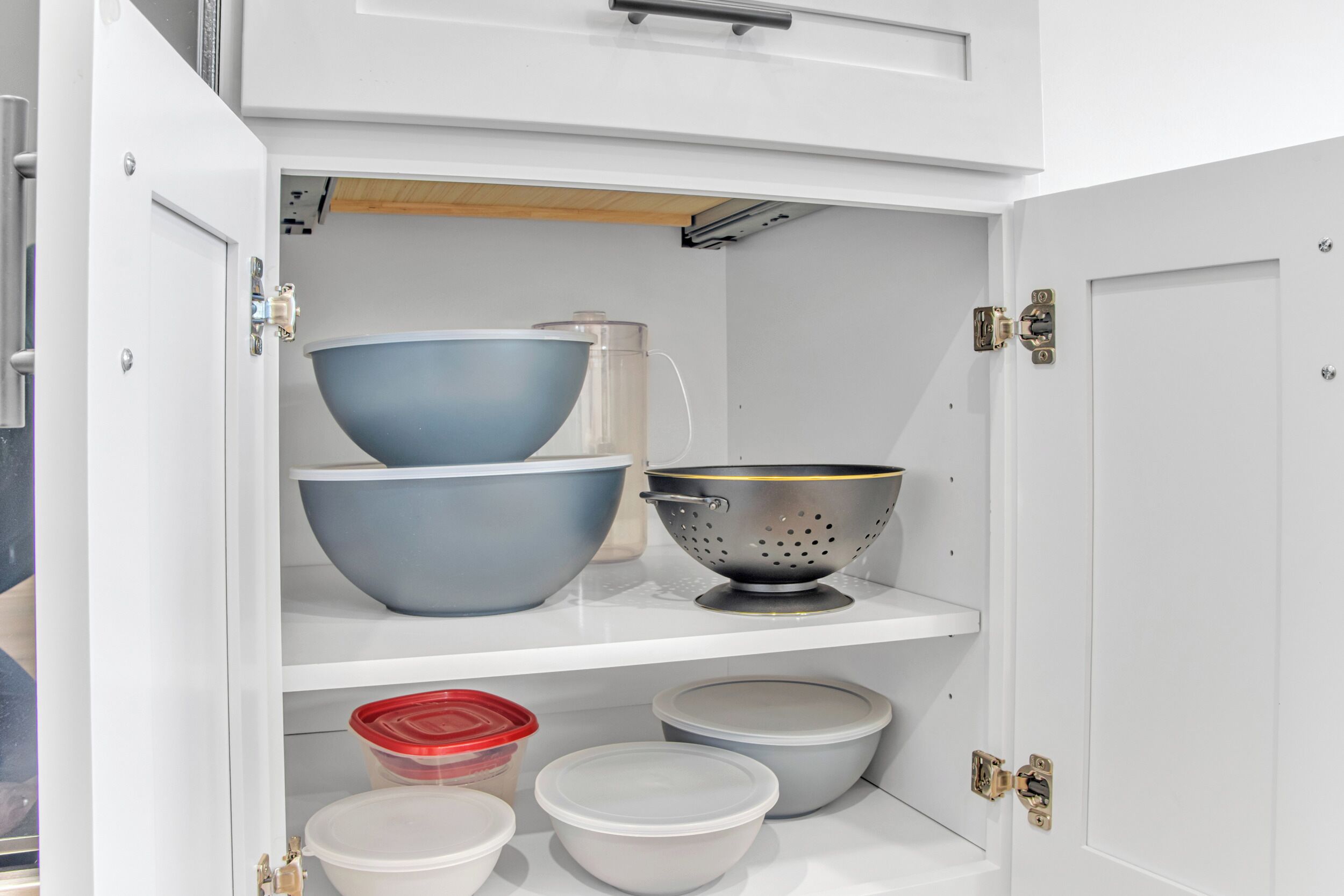 A kitchen cabinet with various storage containers and a colander.
