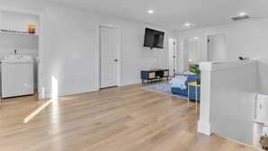 A spacious living area with a wooden floor, a flat-screen TV mounted on the wall, a small side table, and a blue sofa. - Spacious new 3-bedroom house in  Spartanburg (Spartanburg)