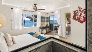 A bedroom with a bed, a nightstand, a window with a view of the ocean, and a ceiling fan.