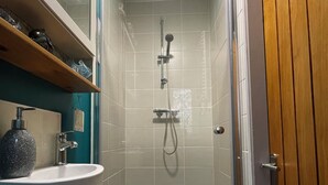 A small bathroom with a shower, a sink, and a wooden door.