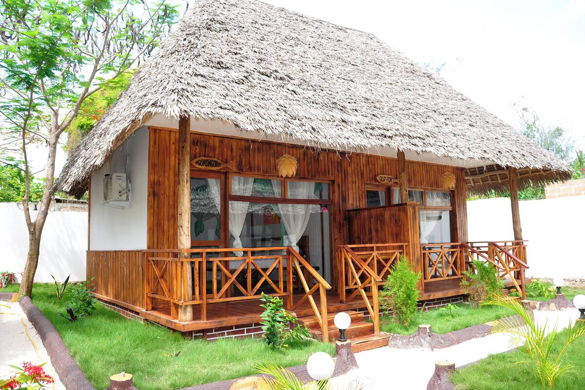Una casa de madera con techo de paja, un porche de madera y un pequeño jardín.