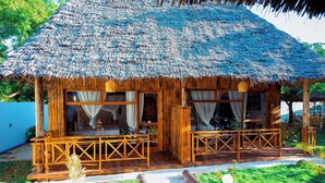 A wooden structure with a thatched roof, large windows, and a wooden porch. - Jodari bungalow kizimkazi Zanzibar (Kizimkazi)