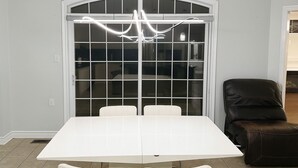 A dining area with a white table and chairs, a black leather chair, and a modern chandelier. - 4 bedroom upper unit in Brampton (Brampton)