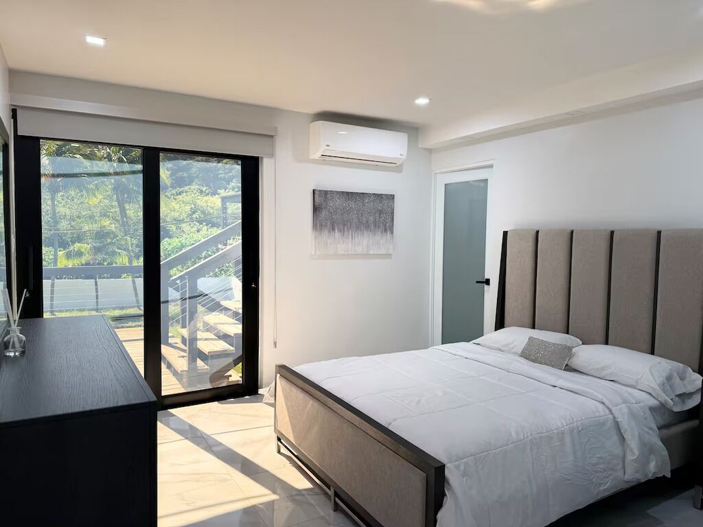 Un dormitorio moderno con una cama grande, un escritorio y un ventanal corredero que da a un balcón.