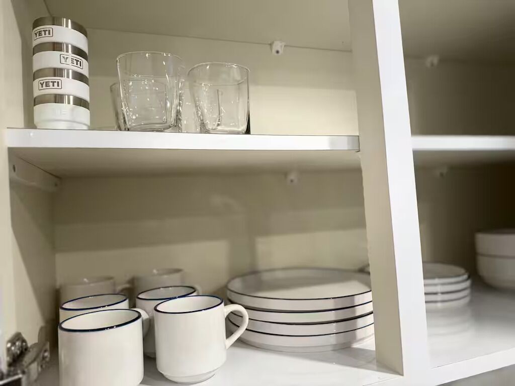 Uma prateleira branca com pratos empilhados, uma caneca e um copo.