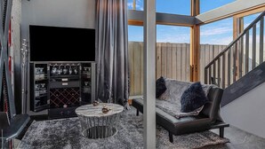 A modern living room with a flat-screen TV, a wine rack, and a sofa with a fur throw. - Sanctuary Hobart CBD (Hobart)