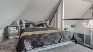 A bedroom with a sloped ceiling, a bed with a patterned bedspread, a bedside table, and a nightstand. - Sanctuary Hobart CBD (Hobart)