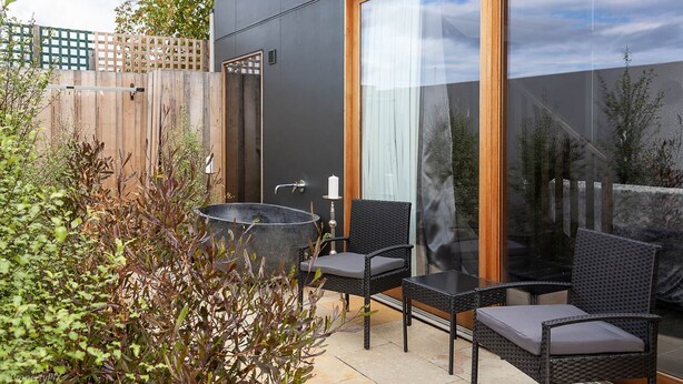 An outdoor patio with a black metal barrel, two wicker chairs, and a table. - Sanctuary Hobart CBD (Hobart)