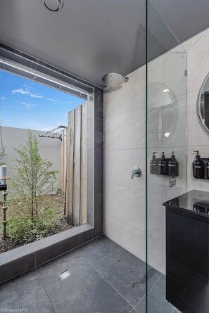 A modern bathroom with a glass shower enclosure, a black sink, and a view of a garden. - Sanctuary Hobart CBD (Hobart)