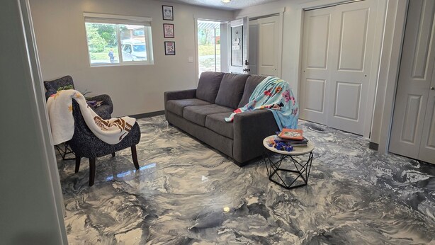 A living room with a marble floor, a gray sofa, a chair with a blanket, and a small table with a bag.