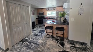 A kitchen with a marble floor, wooden cabinets, a microwave, a refrigerator, and a small island with stools.