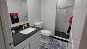 A bathroom with a marble floor, a white toilet, a sink with a mirror above it, and a shower area.