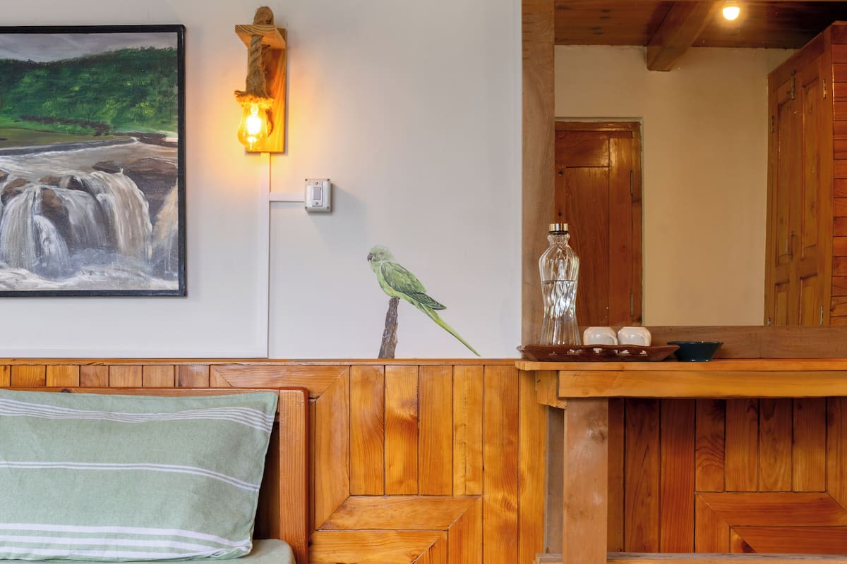 A wooden bed with a green pillow, a nightstand with a lamp, a framed painting of a waterfall, and a wooden cabinet with a mirror.