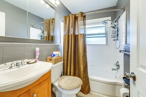 A bathroom with a white sink, toilet, and bathtub. There is a shower curtain and a window above the bathtub. - Game, Stay & Play: Family Home in Westland! (Westland)