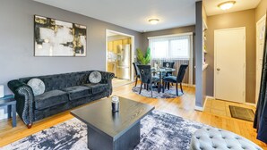 Een moderne woonkamer met een donkergrijze bank, een salontafel, en een eethoek met een ronde tafel en stoelen.