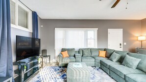 Een moderne woonkamer met een hoekbank, een flatscreen televisie en een plafondventilator.