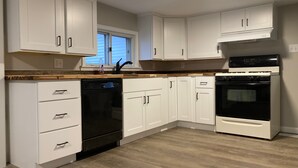 Una cocina moderna con armarios blancos, un lavavajillas negro, un horno negro y una encimera de madera.