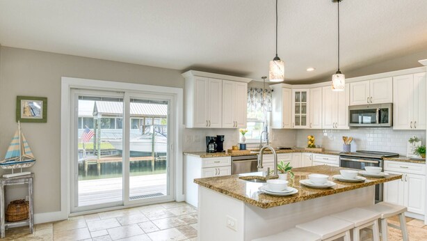A kitchen with white cabinets, a granite countertop, a sink, a microwave, and a dining area with stools. - Heated Pool, Walk to Beach, 40’ Boat Dock, Kayak, Paddle Board, Fishing, $300 in Free Tickets! (St. Augustine)