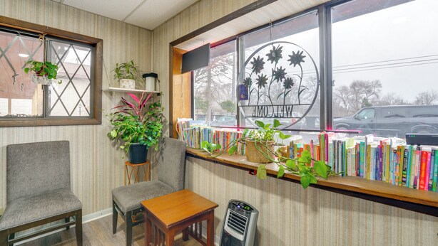A cozy room with a wooden table, a chair, a bookshelf filled with books, and a window with a view of the street. - Pet-Friendly Studio Near Pine Knob: Bring Skis! (Village of Clarkston)