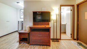 Ein Hotelzimmer mit einem Holztisch, einem Flachbildfernseher, einer Lampe und einer Tür zu einem Badezimmer.
