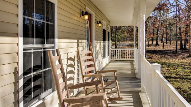 Une véranda avec des fauteuils à bascule en bois et une balustrade blanche.