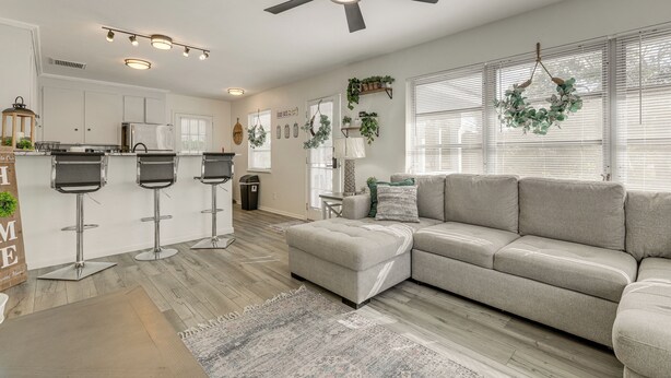 A modern living room with a sectional sofa, a ceiling fan, and a kitchen area with bar stools. - Walk to Shops & Dining: Downtown Stuart Home! (Stuart)