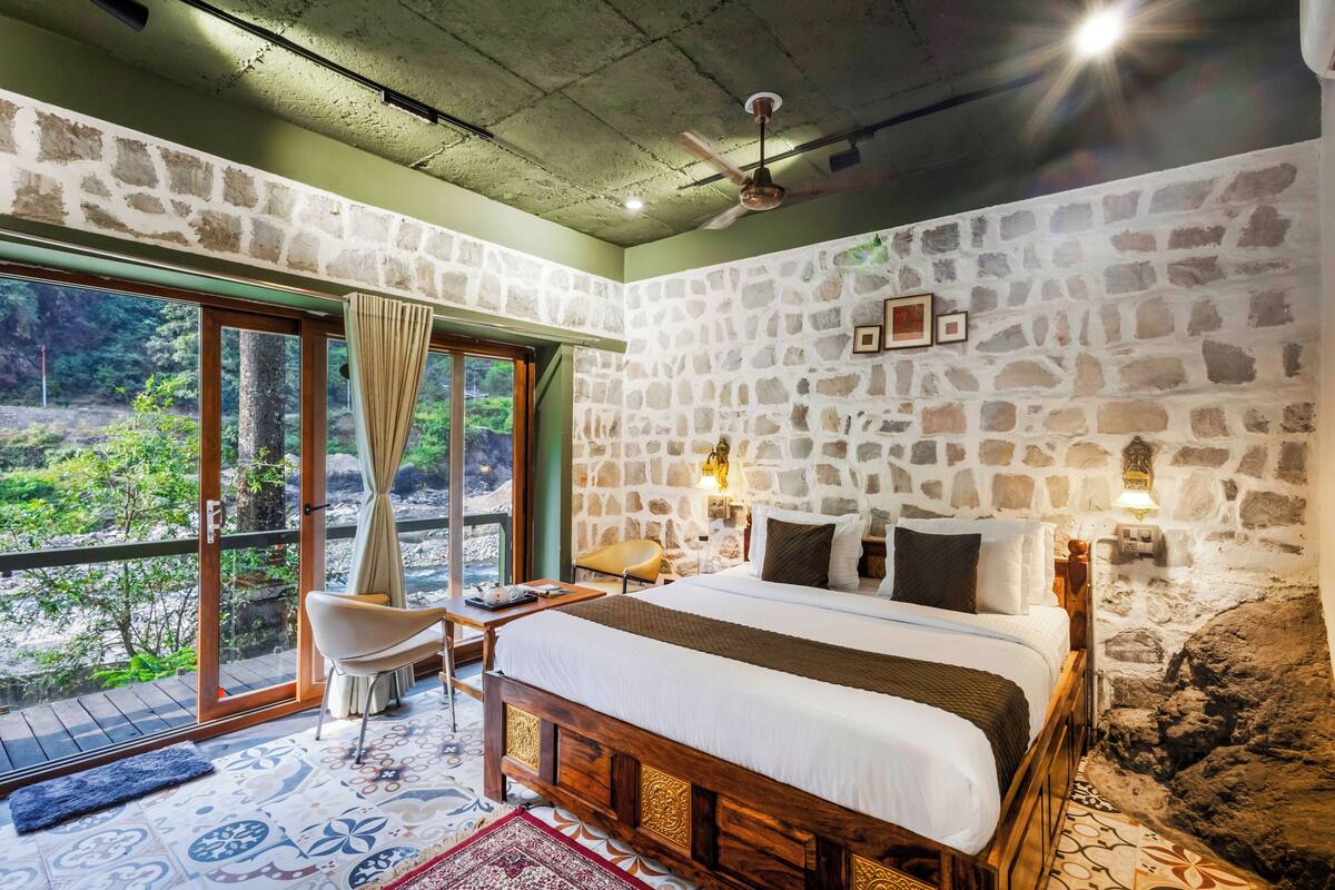 A bedroom with a stone wall, a bed, a desk, and a chair.