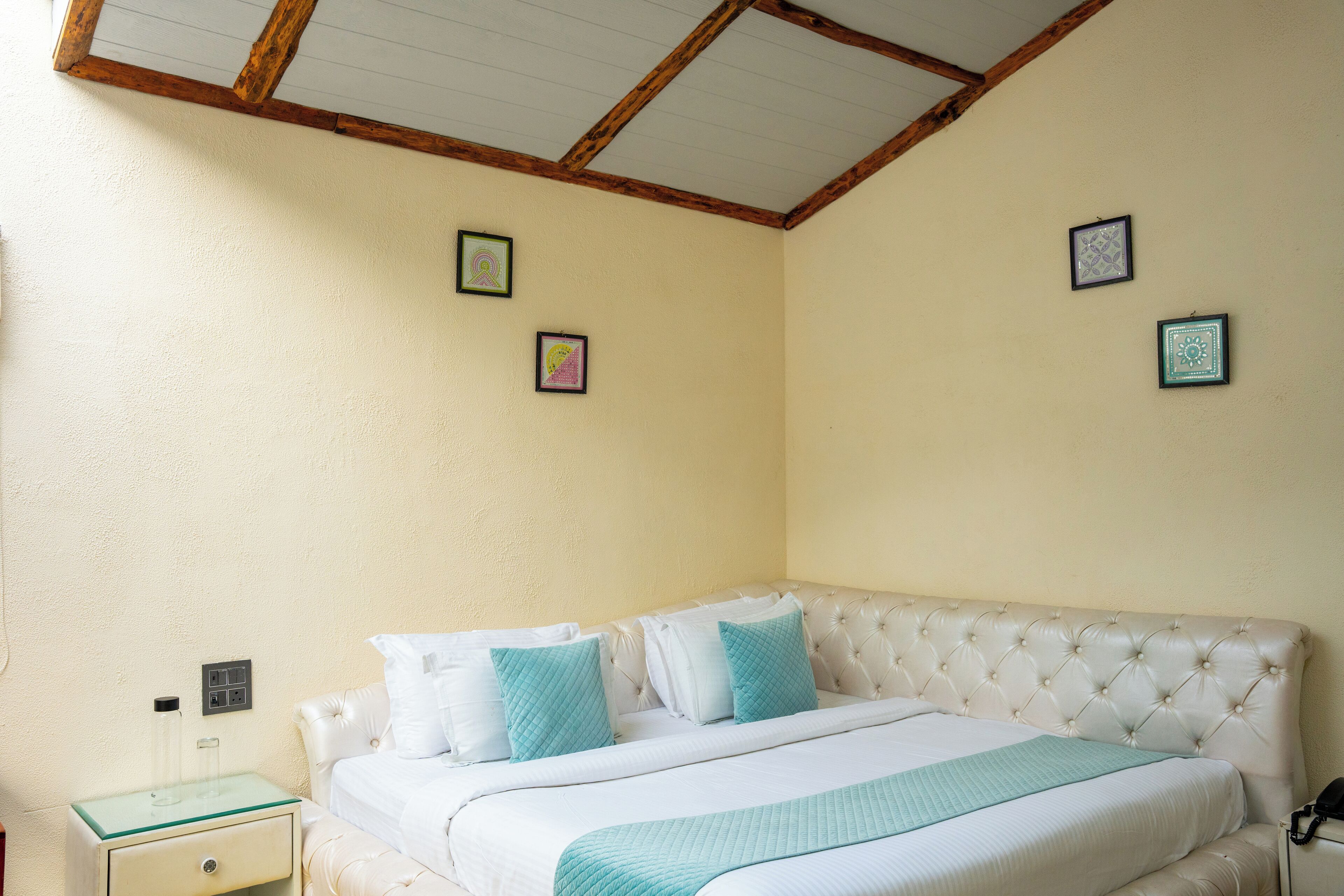A bedroom with a tufted headboard, a glass bedside table, and a bed with white and teal bedding.