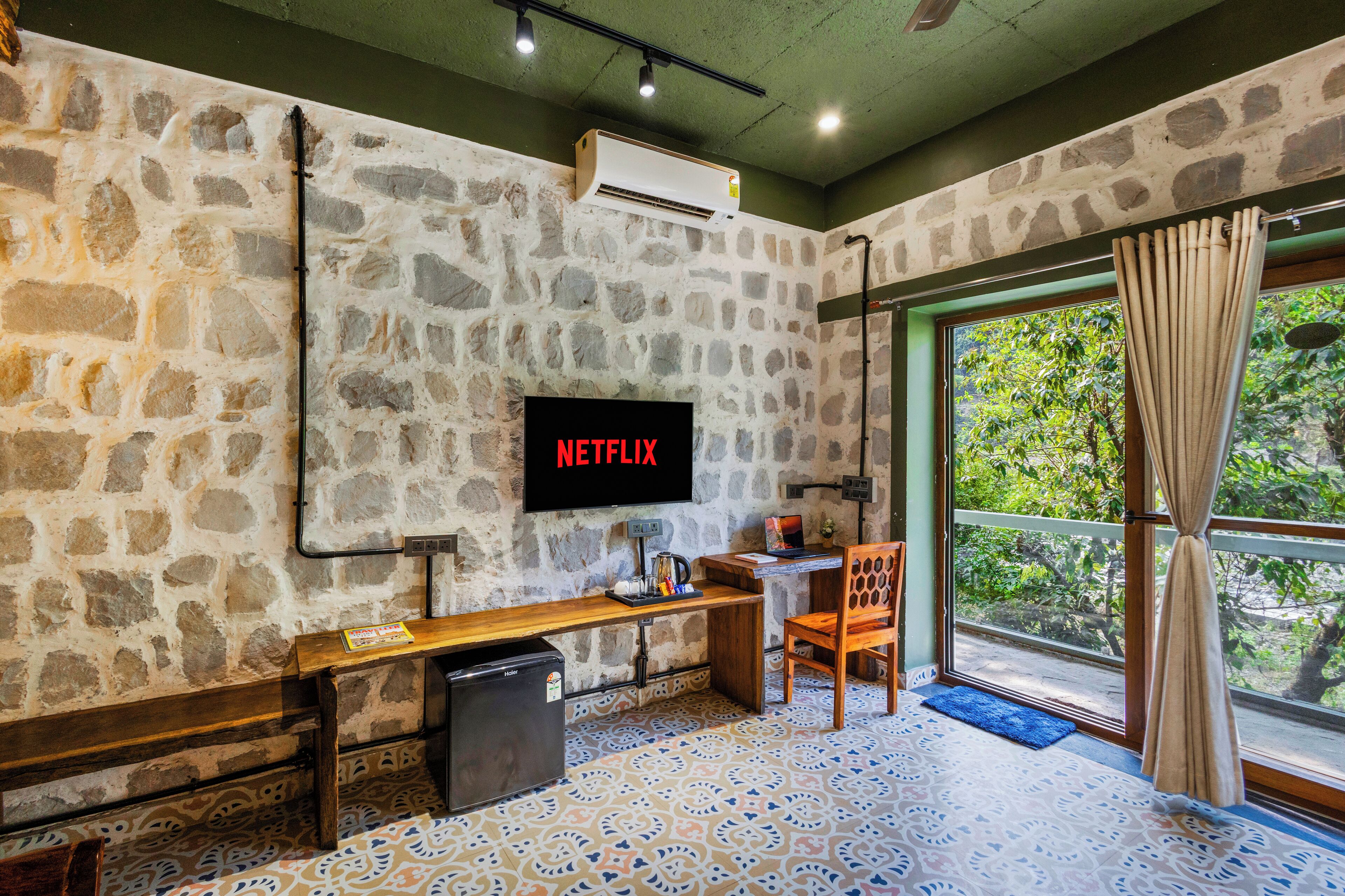 Habitación con paredes de piedra, televisor, escritorio, silla y ventana con cortinas.