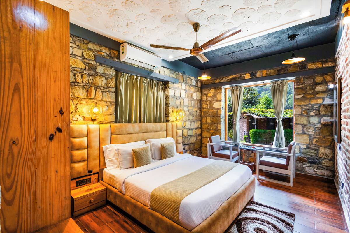 A bedroom with a stone wall, a large bed, a ceiling fan, and a view of the outdoors.