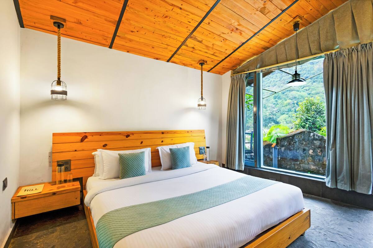 A bedroom with a wooden headboard, a large bed with white and green bedding, two bedside lamps, a nightstand, and a window with curtains.