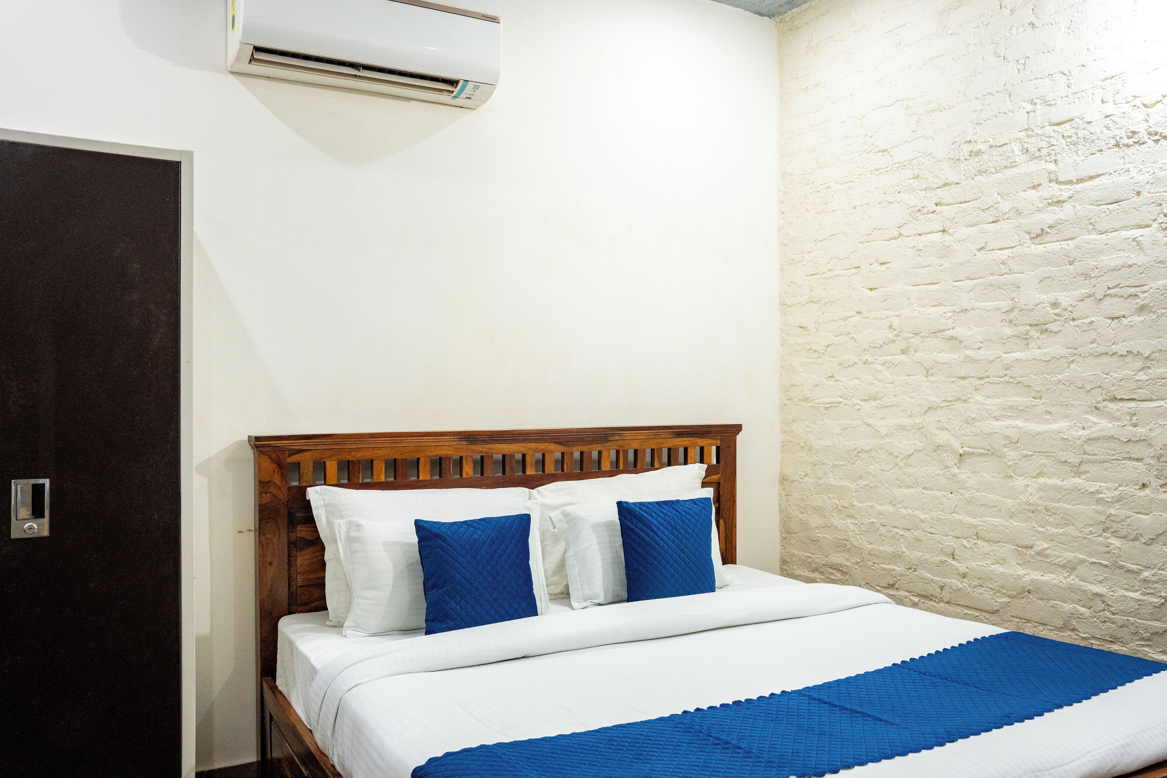 A bedroom with a wooden bed, white bedding, and a blue accent pillow.