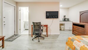 A bedroom with a bed, a desk with a chair, a TV, a microwave, and a wardrobe.