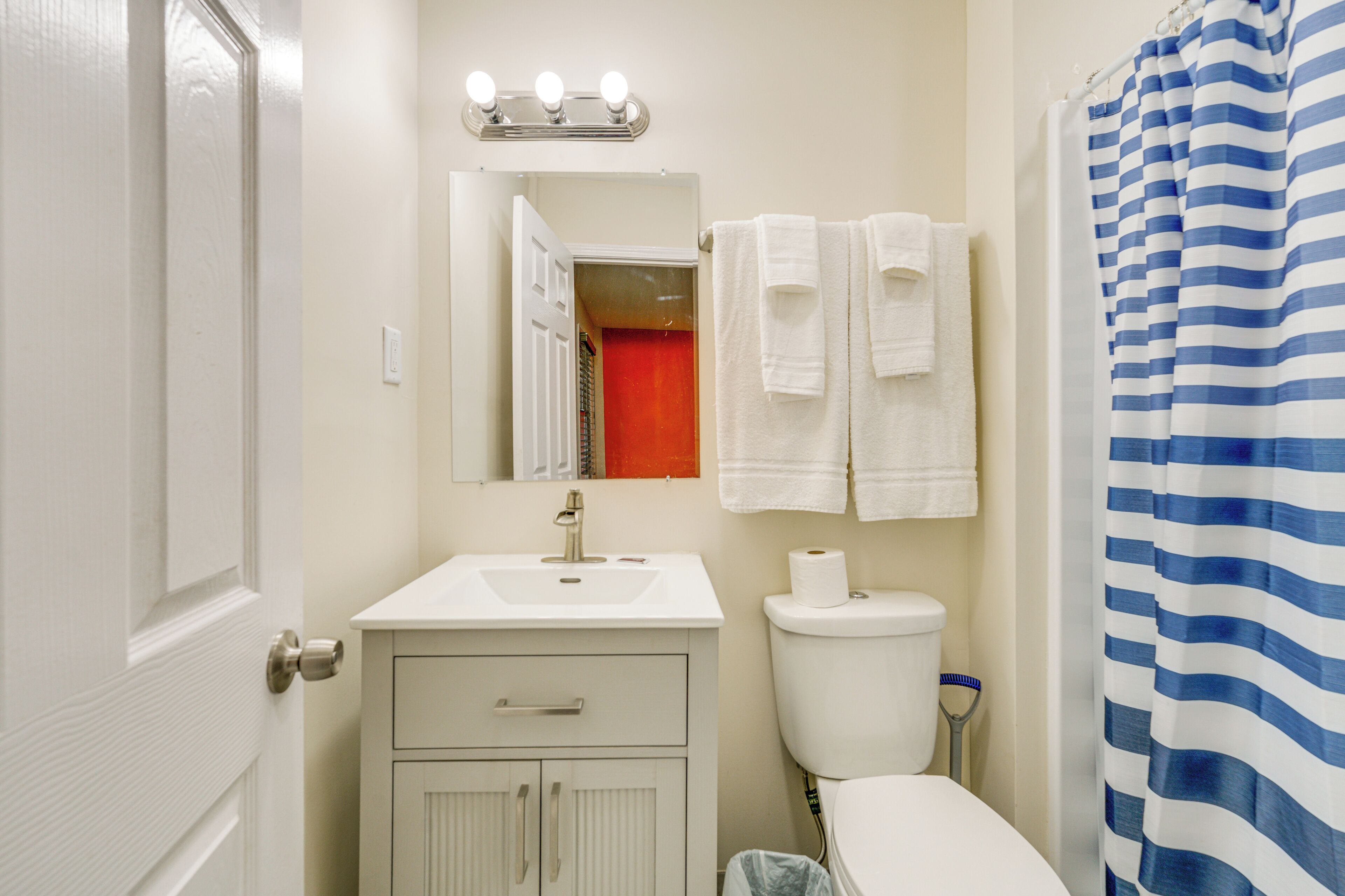 Une salle de bain avec un lavabo blanc, des toilettes, un miroir avec éclairage et un rideau de douche à rayures.