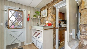 A room with a door, a small shelf with plants, a fire extinguisher, and a stone wall.