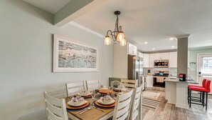 Un coin repas avec une table en bois dressée pour quatre personnes, des chaises blanches et un lustre.