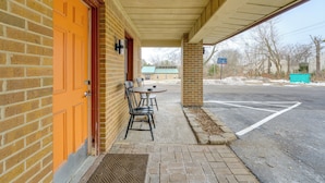 Un bâtiment en briques avec une porte orange, un patio couvert avec une table et des chaises, et un parking en arrière-plan.