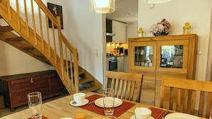 A dining area with a wooden table set for four, a staircase, and a kitchen in the background. - Vacation home Rügentraum with fireplace and sauna in TOP location (Glowe)