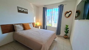 Een slaapkamer met een bed, een nachtkastje, een raam met gordijnen en een spiegel aan de muur.
