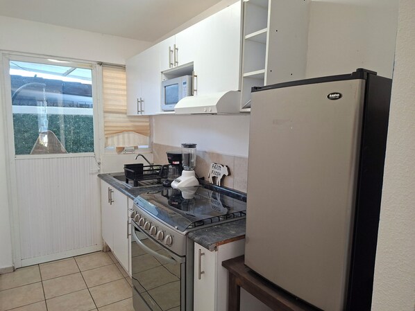 A compact kitchen with a stove, microwave, and refrigerator. - Casa Veta by Avelia (Corregidora)