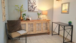 Een kamer met een fauteuil, een houten kast met glazen deuren, een bijzettafeltje en een spiegel aan de muur.