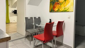 A dining area with a glass table, red and grey chairs, a painting of flowers on the wall, and a visible bathroom door. - Long Stay 1BR Apt Near Prater Park (Vienna)