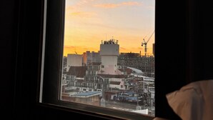 Vista desde una ventana con vista a un paisaje urbano al atardecer, donde se ven edificios y grúas de construcción.