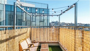 Terraza en la azotea con vistas a la ciudad, que incluye un muro de cristal, una valla de bambú e iluminación con guirnaldas.
