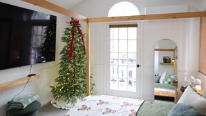 A cozy room with a Christmas tree, a bed with a patterned blanket, a TV, and a window with blinds. - Welcome to my Mushroom Cottage Enjoy this cozy & Unique  Home (Big Bear)
