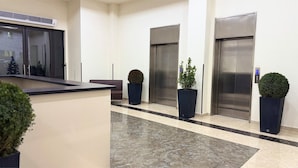 Een receptiezone met een balie, twee liften en potplanten.