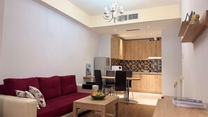 Een moderne woonkamer met een rode bank, een houten salontafel en een eethoek, met een keuken op de achtergrond.
