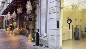 Een hotelentree met een kerstboom versierd met lichtjes en decoraties, een bord met het adres, en een glazen deur met een bord waarop staat 