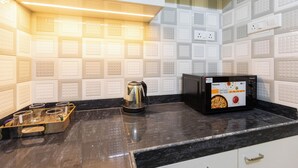 A kitchen with white tiled backsplash, a black countertop, a coffee maker, and a microwave. - City Haven by Jadecaps Nr. Belle Vue Hsp 3bhk (Kolkata)